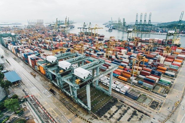 Utsikt ovanifrån över en stor hamn fylld med containrar i olika färger och lyftkranar.