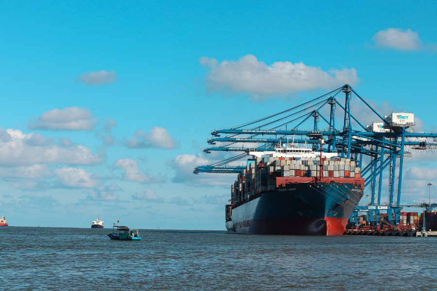 A large cargo ship docked at a port, being loaded with containers by cranes.