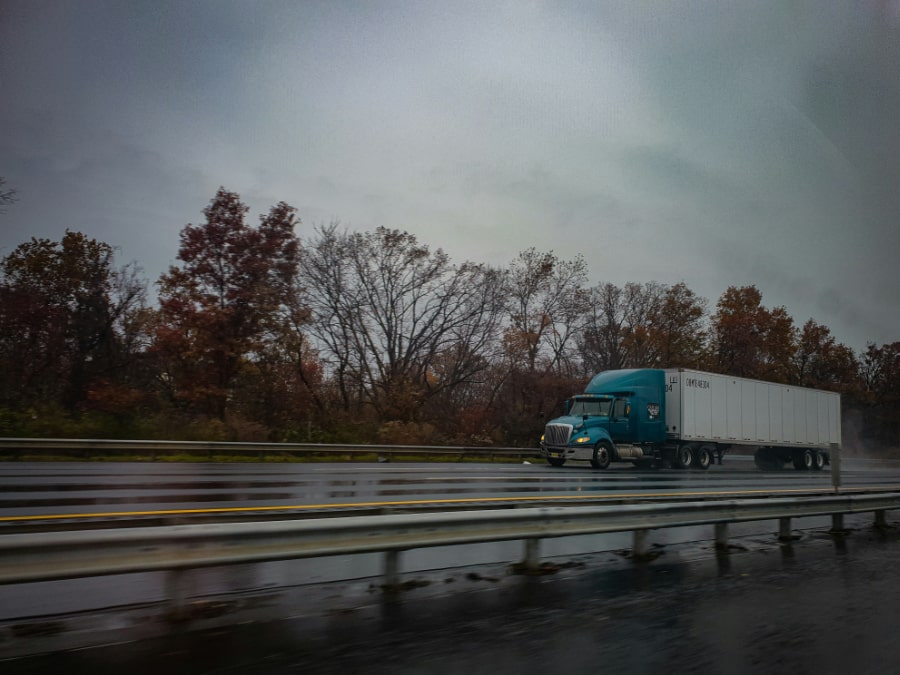 A blue truck drives on a highway, surrounded by autumn-colored trees