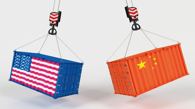 Two containers hanging from four chains. The blue container on the left has the US flag on the front, while the orange container on the right has the China flag on the front.